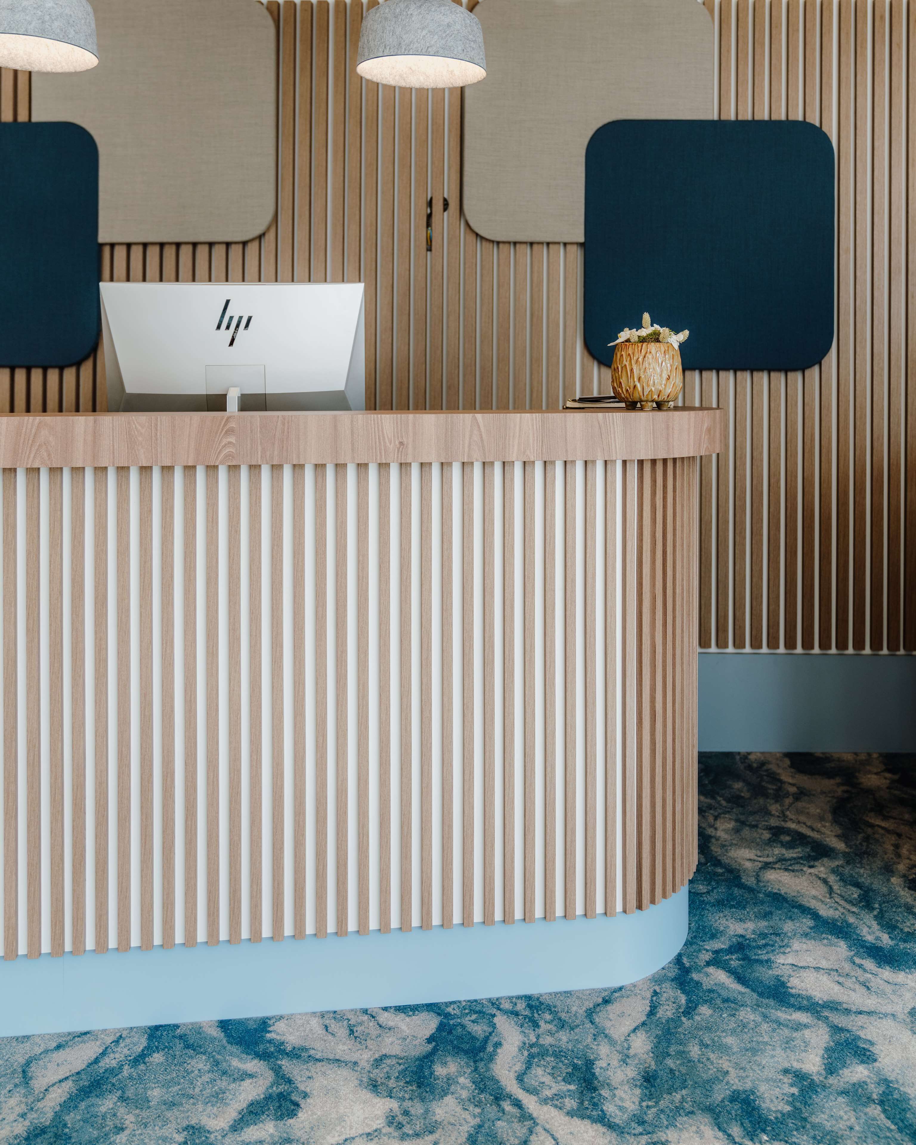 A reception desk with vertical wooden slats, a white sign with black text, and a decorative vase.