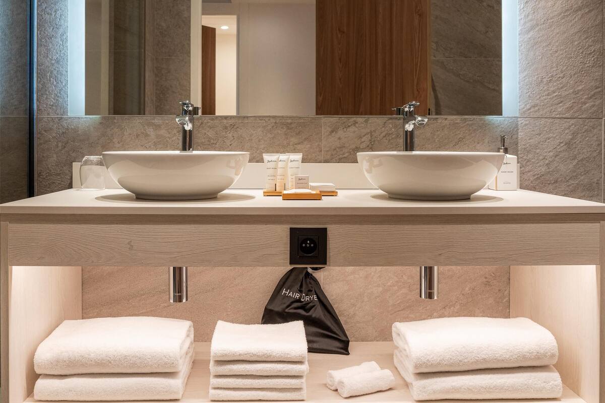 A modern bathroom with two sinks, a large mirror, and a towel rack.