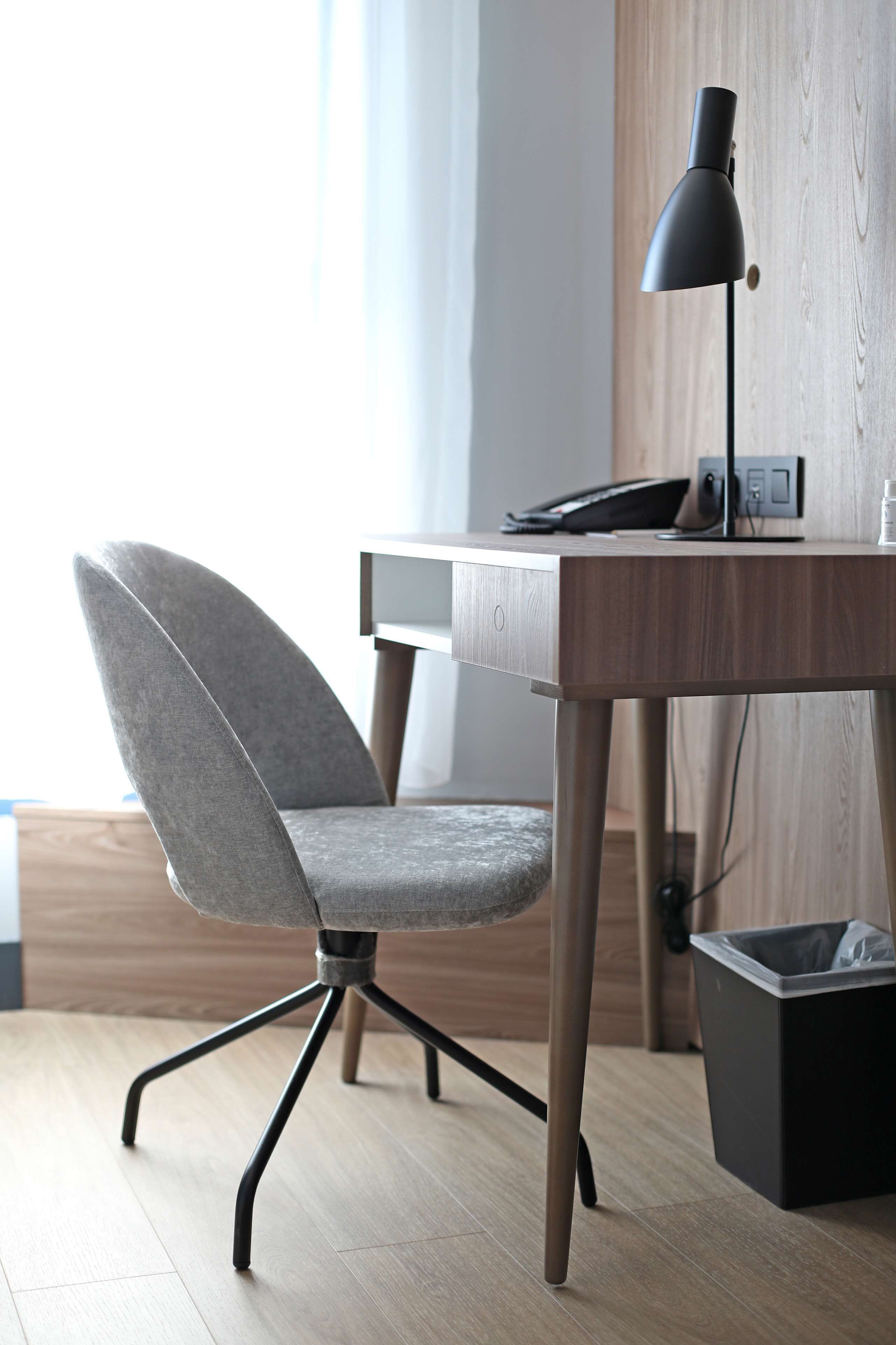 Un fauteuil de bureau moderne avec un siège en tissu gris et un bureau en bois équipé d’une lampe de bureau noire.