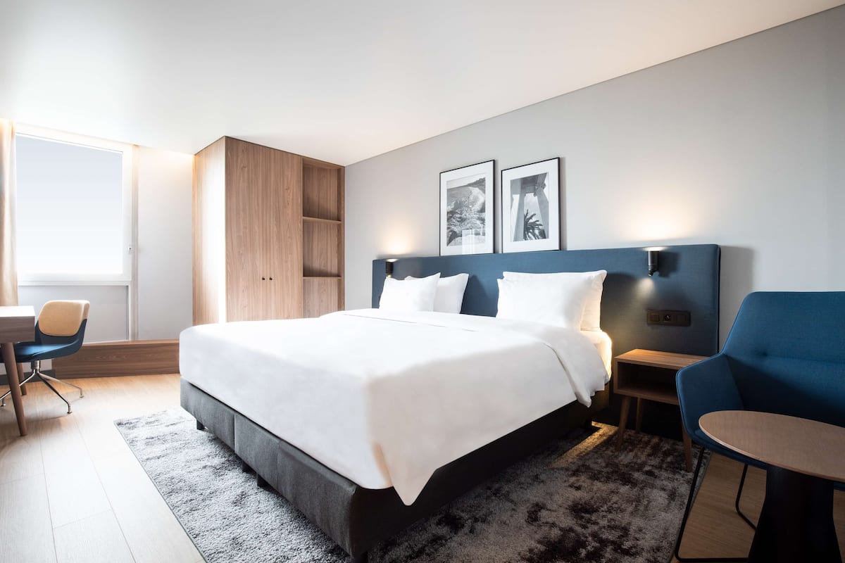 A modern bedroom with a large bed, a desk, a chair, and a wardrobe.