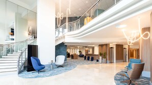 A modern lobby with a curved reception desk, seating areas, and a staircase leading to upper floors. - Radisson Hotel Nice Airport (Nice)