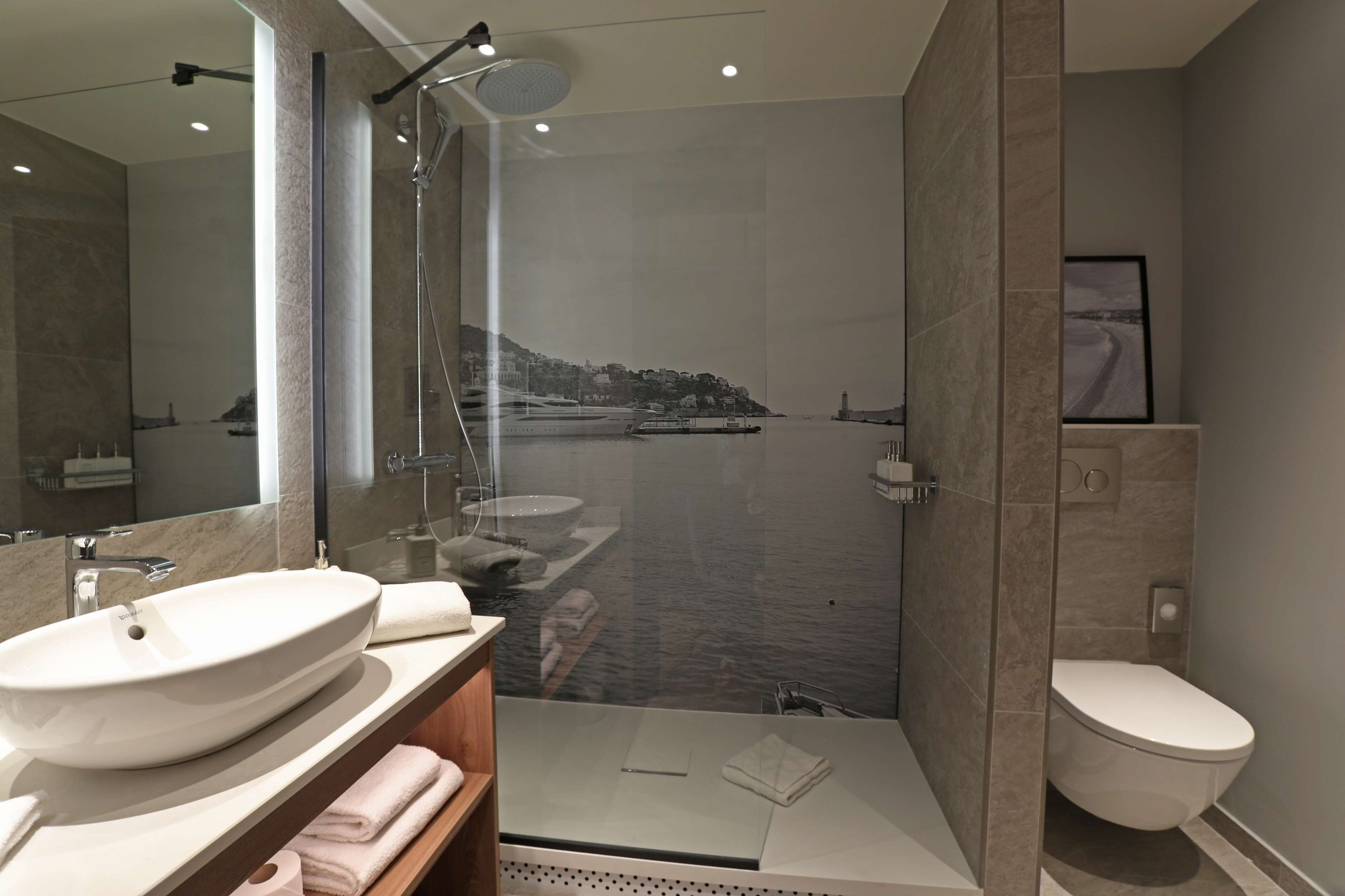 A modern bathroom with a large mirror, a white sink, a glass-enclosed shower, and a toilet.