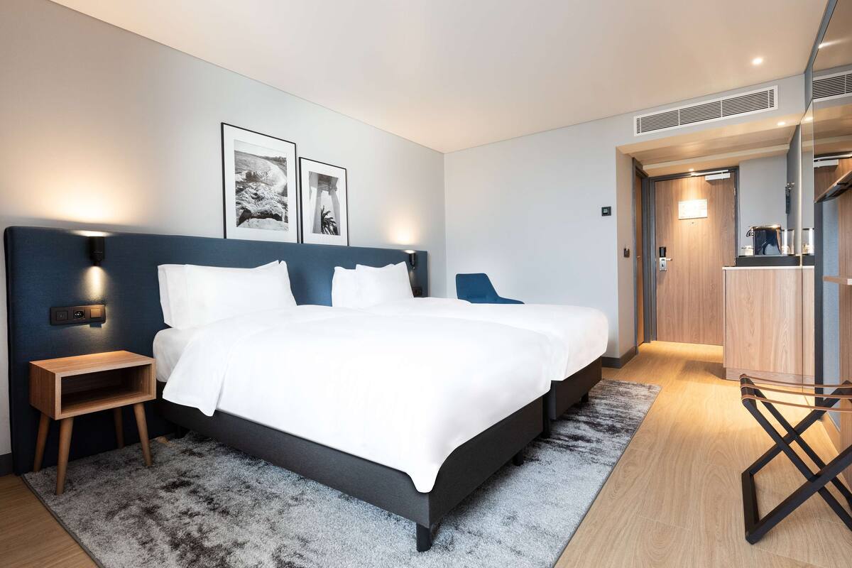 A modern hotel room with a large bed, bedside tables, and a wardrobe.