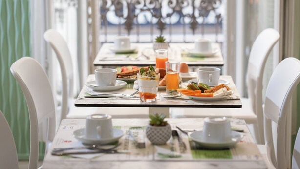 Un desayuno con sillas blancas, una mesa dispuesta con platos, tazas y un vaso de jugo de naranja.