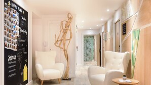 Un moderno vestíbulo de hotel con dos sillones blancos, una escultura de madera y una pared decorada con fotografías y texto.