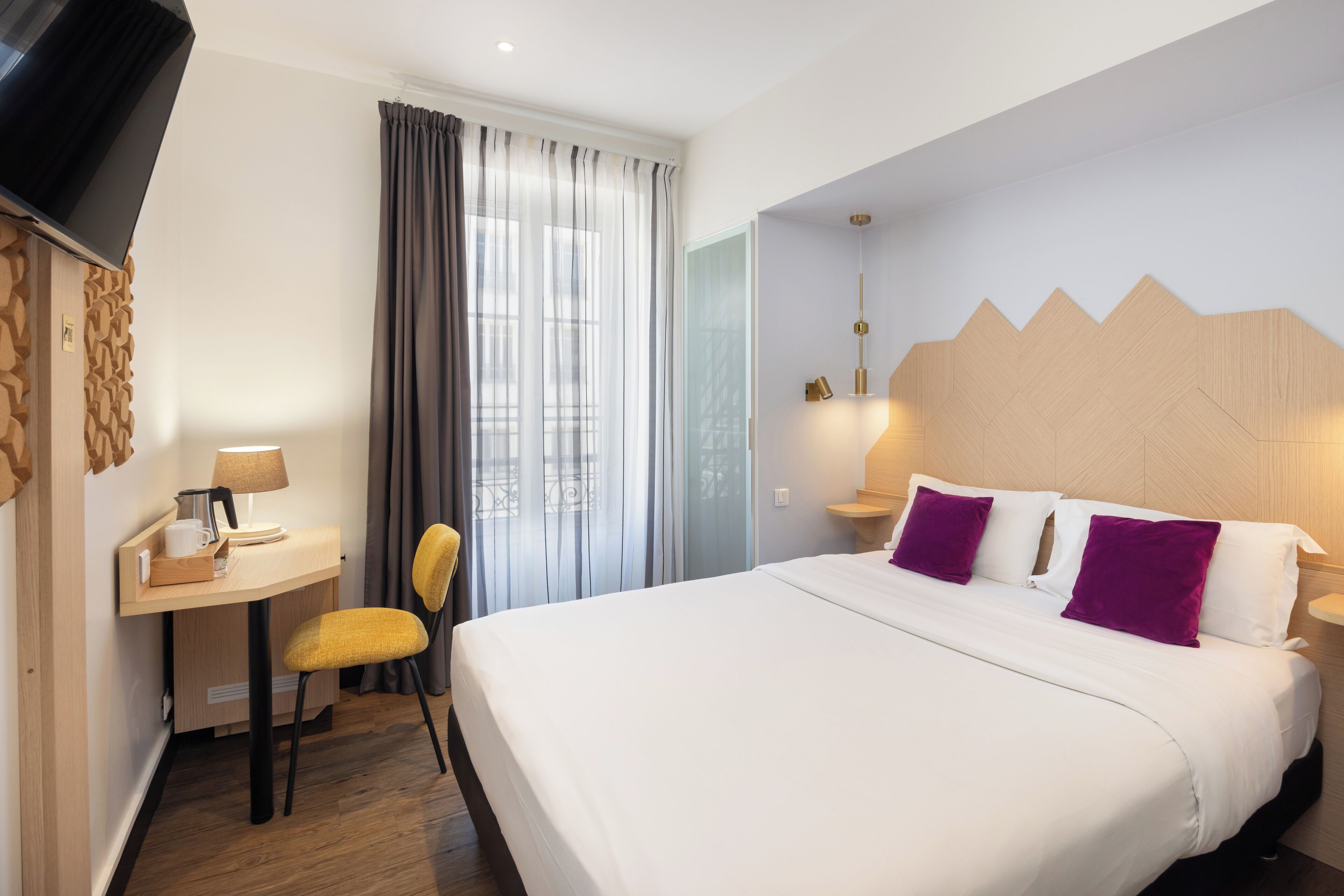 A hotel room with a bed, a desk, a chair, a TV, and a window with curtains.