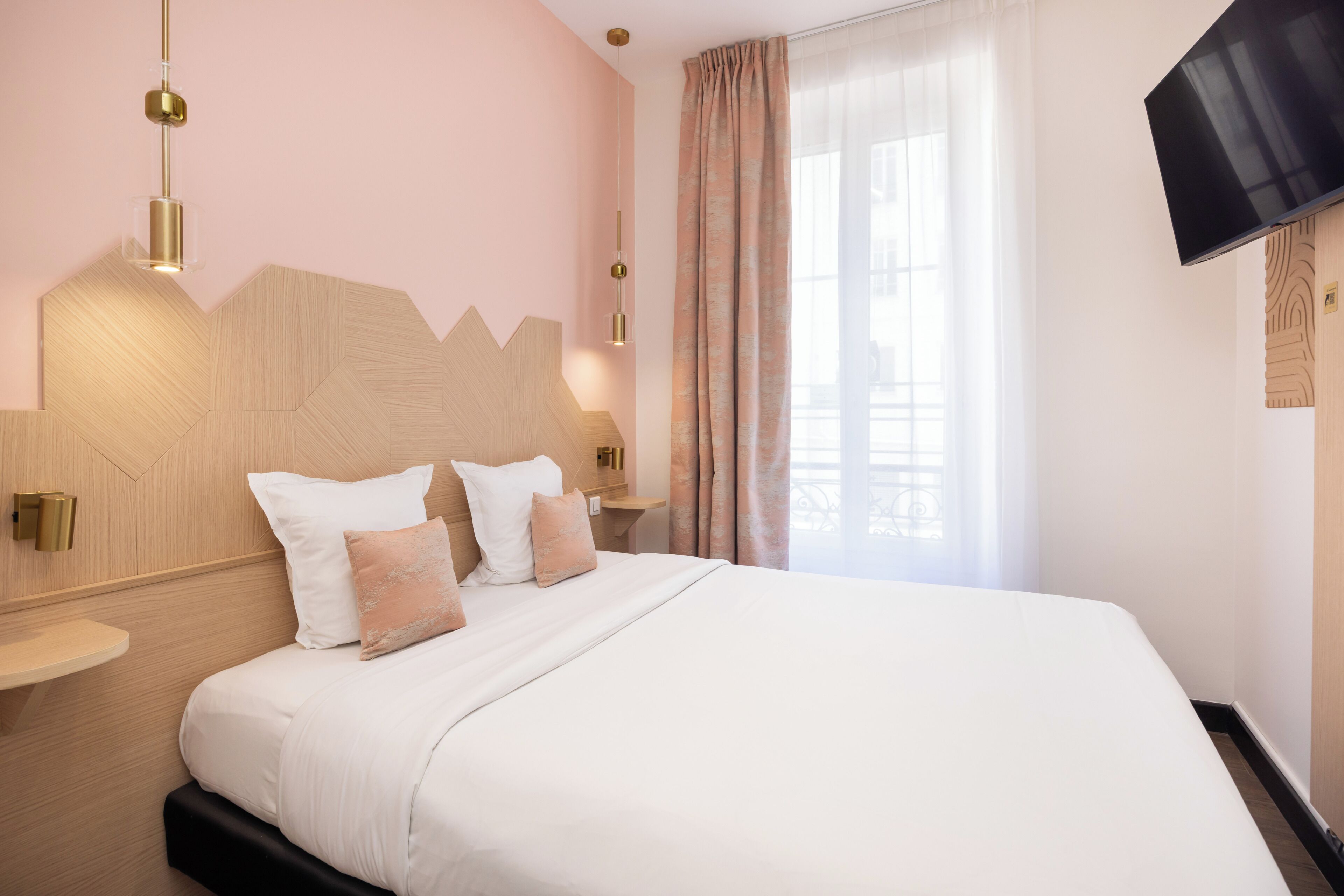 Una habitación de hotel con una cama grande, un televisor montado en la pared y una mesita de noche.