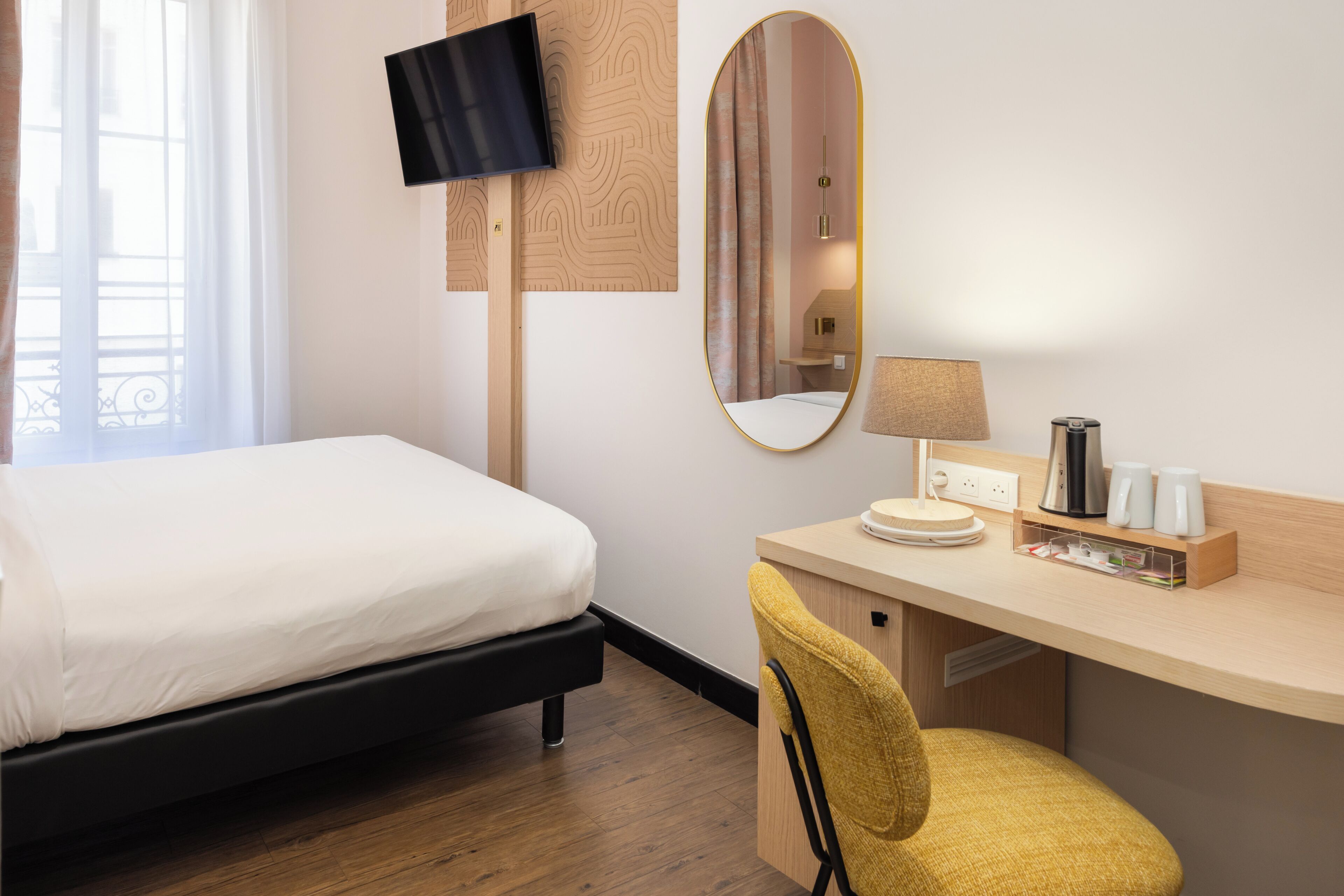 A hotel room with a bed, a desk with a chair, a TV, a mirror, and a lamp.