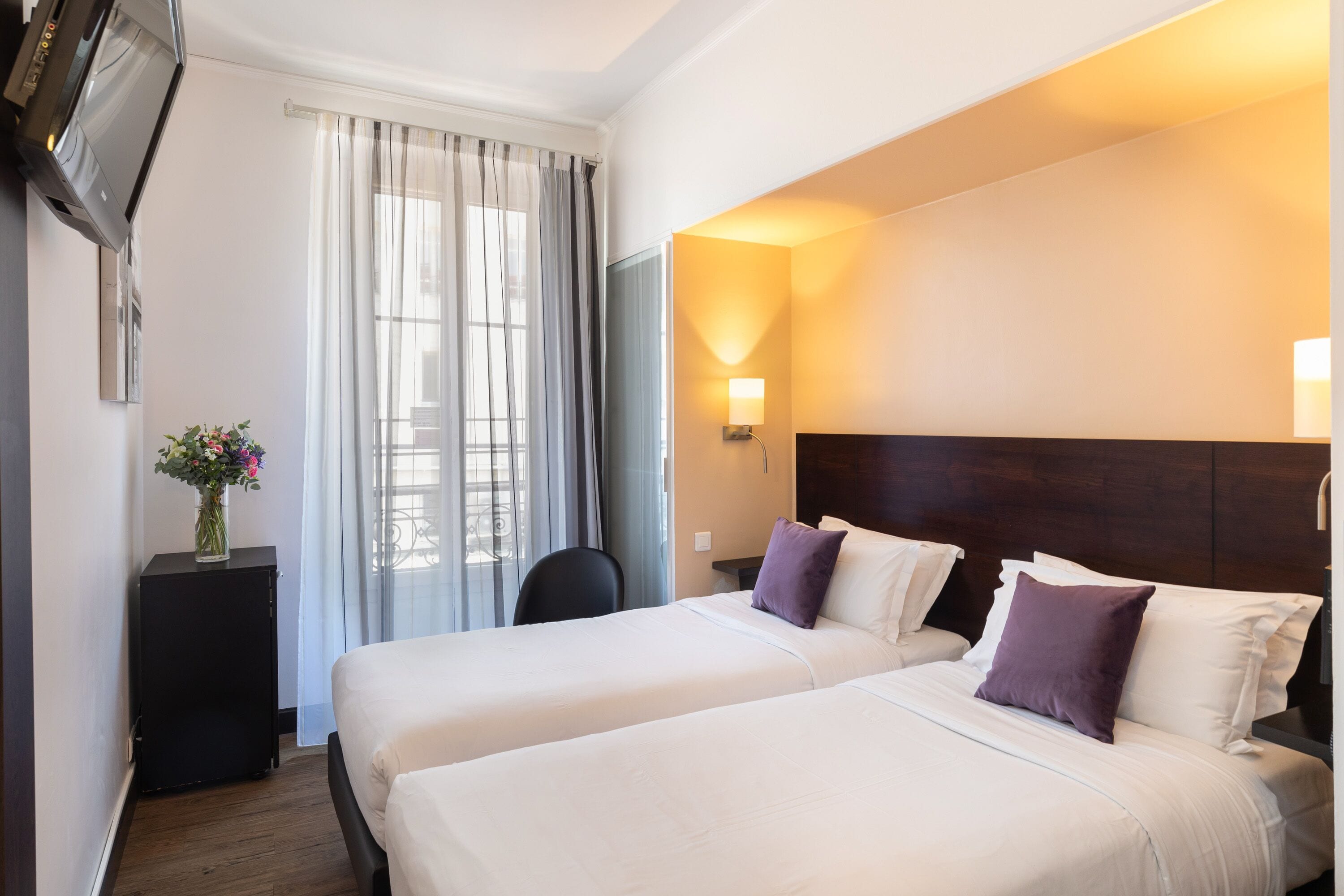 A hotel room with two beds, a desk, a chair, a TV, and a window with curtains.