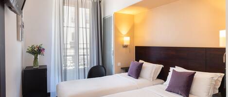 A hotel room with two beds, a desk, a chair, a TV, and a window with curtains.