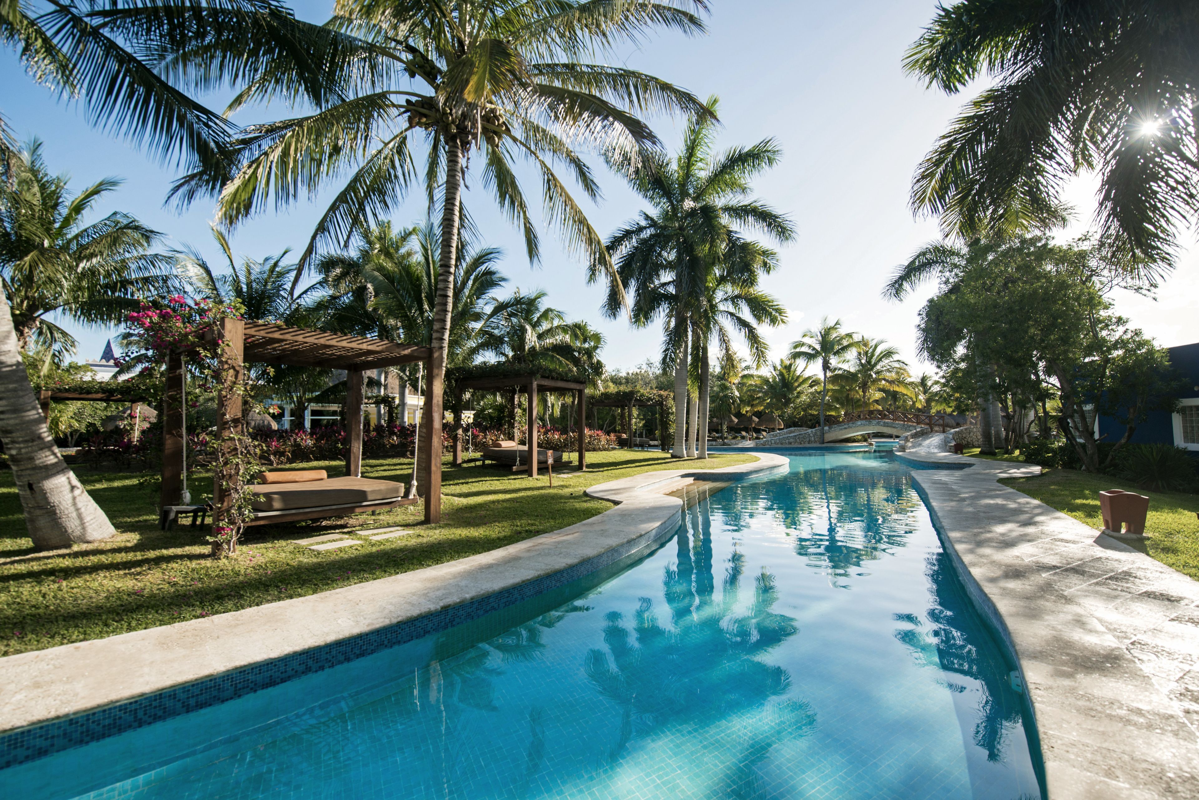 Una piscina con superficie d'acqua cristallina azzurra, circondata da palme e un gazebo.