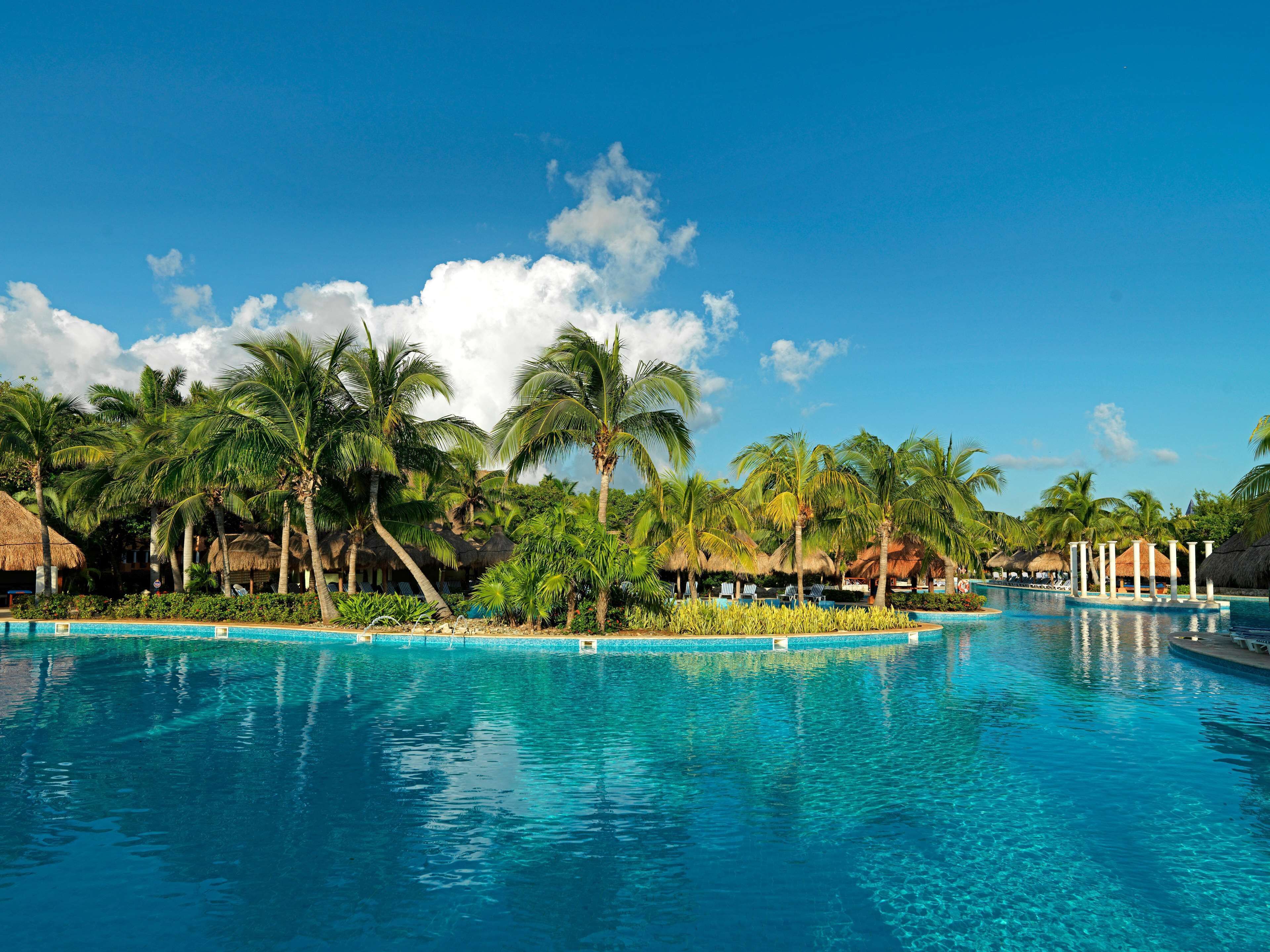 Een resort zwembad omringd door palmbomen en hutten met rieten daken.