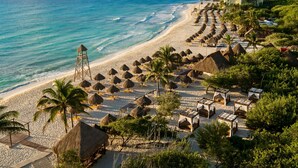 A beach resort with thatched-roof huts, palm trees, and a clear view of the ocean.
