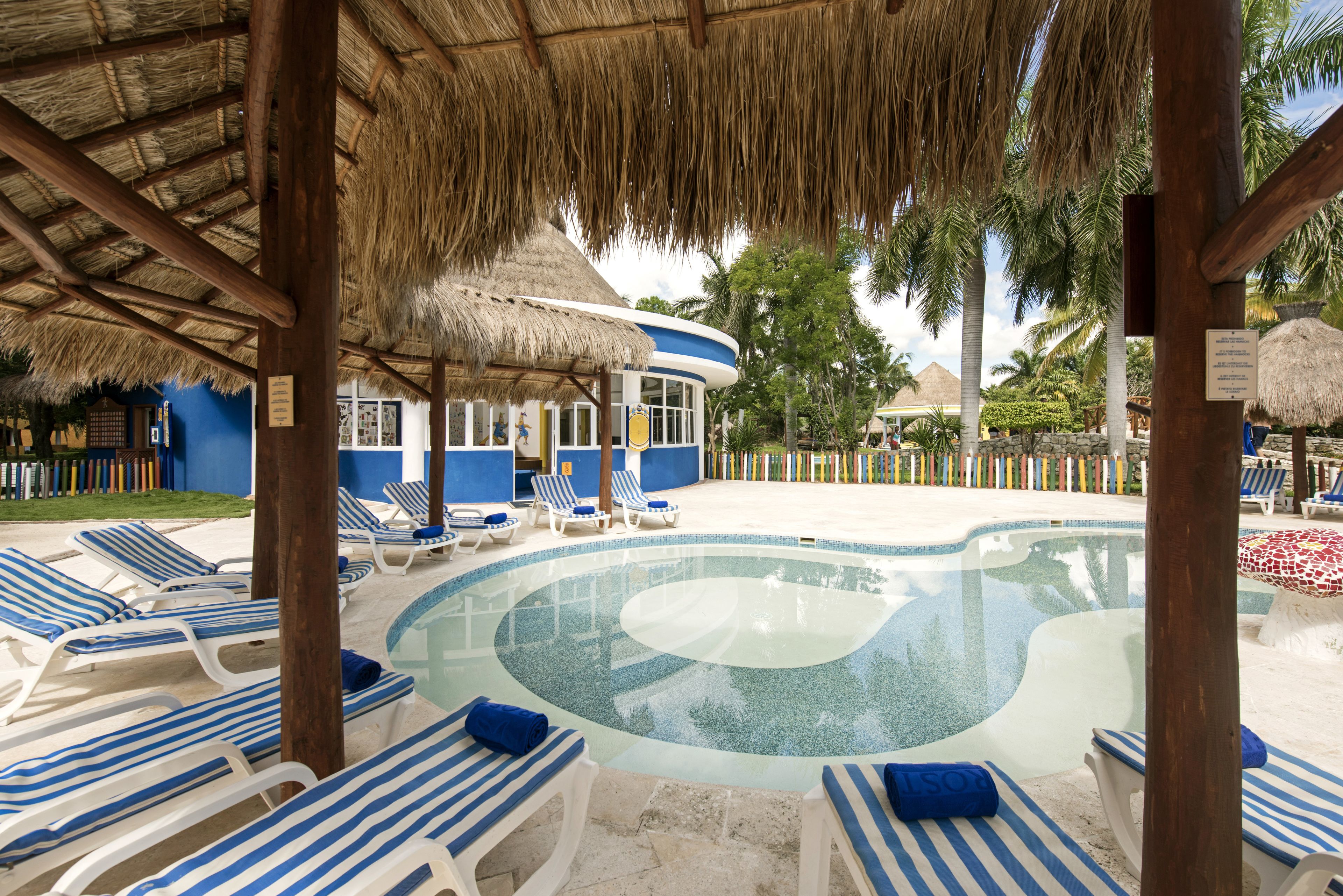 A pool area with lounge chairs and a thatched-roof structure.