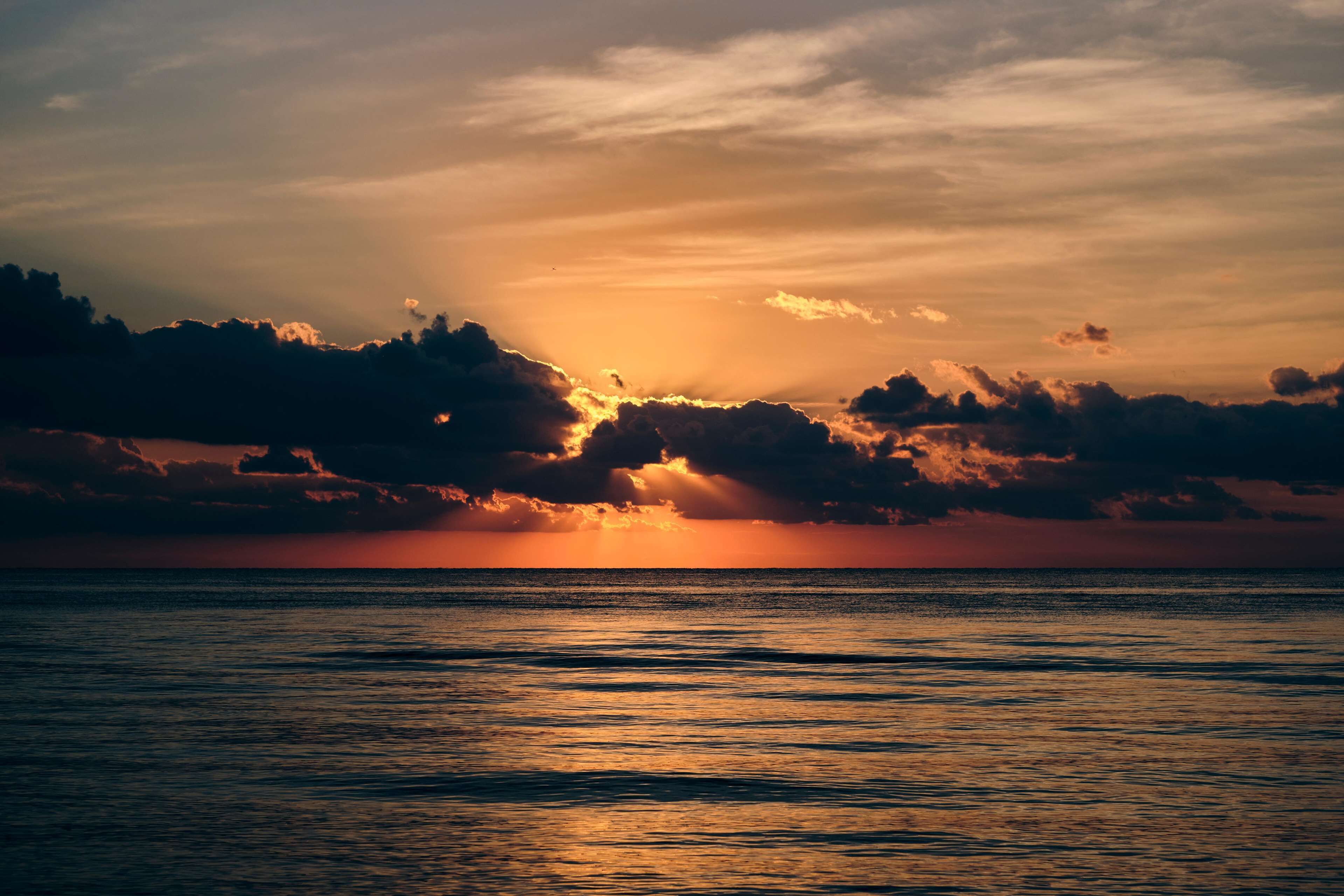 Ein Sonnenuntergang über ruhigem Meer, wobei sich Wolken im Wasser spiegeln.