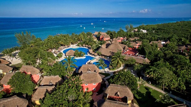 A resort with a central swimming pool, thatched-roof buildings, and a view of the ocean. - Iberostar Waves Cozumel - All Inclusive (Cozumel)
