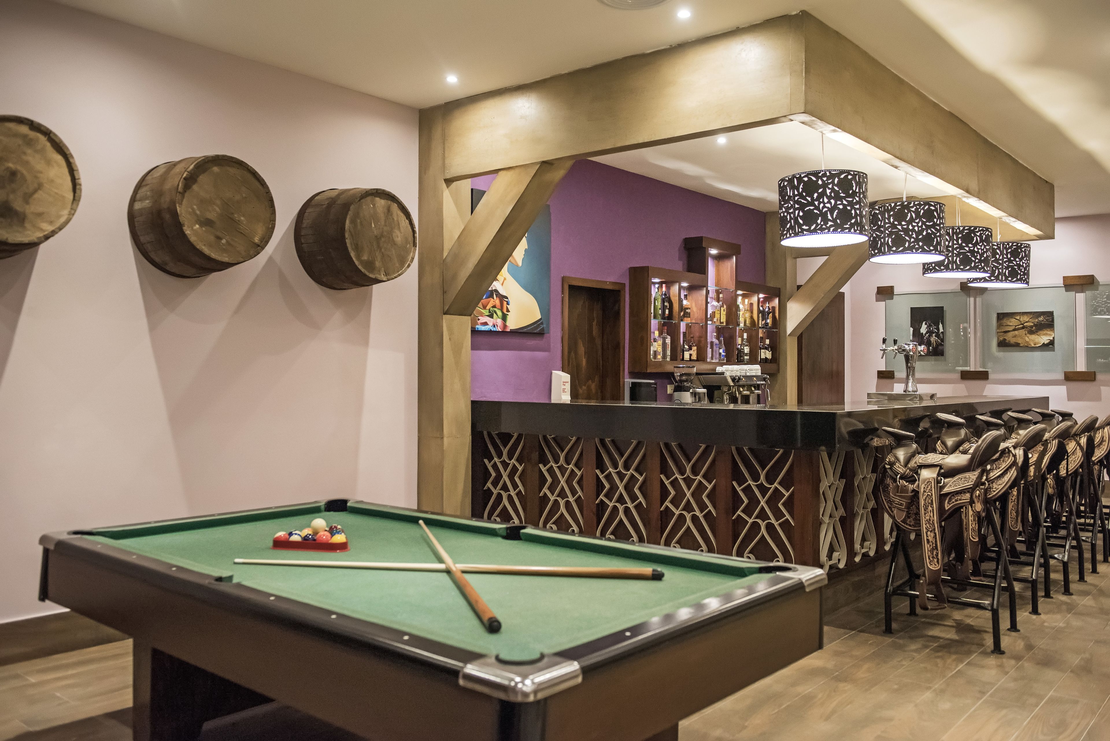 Une table de billard avec des queues et des billes, un coin bar avec des tabourets et un mur décoratif agrémenté d’éléments en bois.