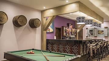 Une table de billard avec des queues et des billes, un coin bar avec des tabourets et un mur décoratif agrémenté d’éléments en bois.