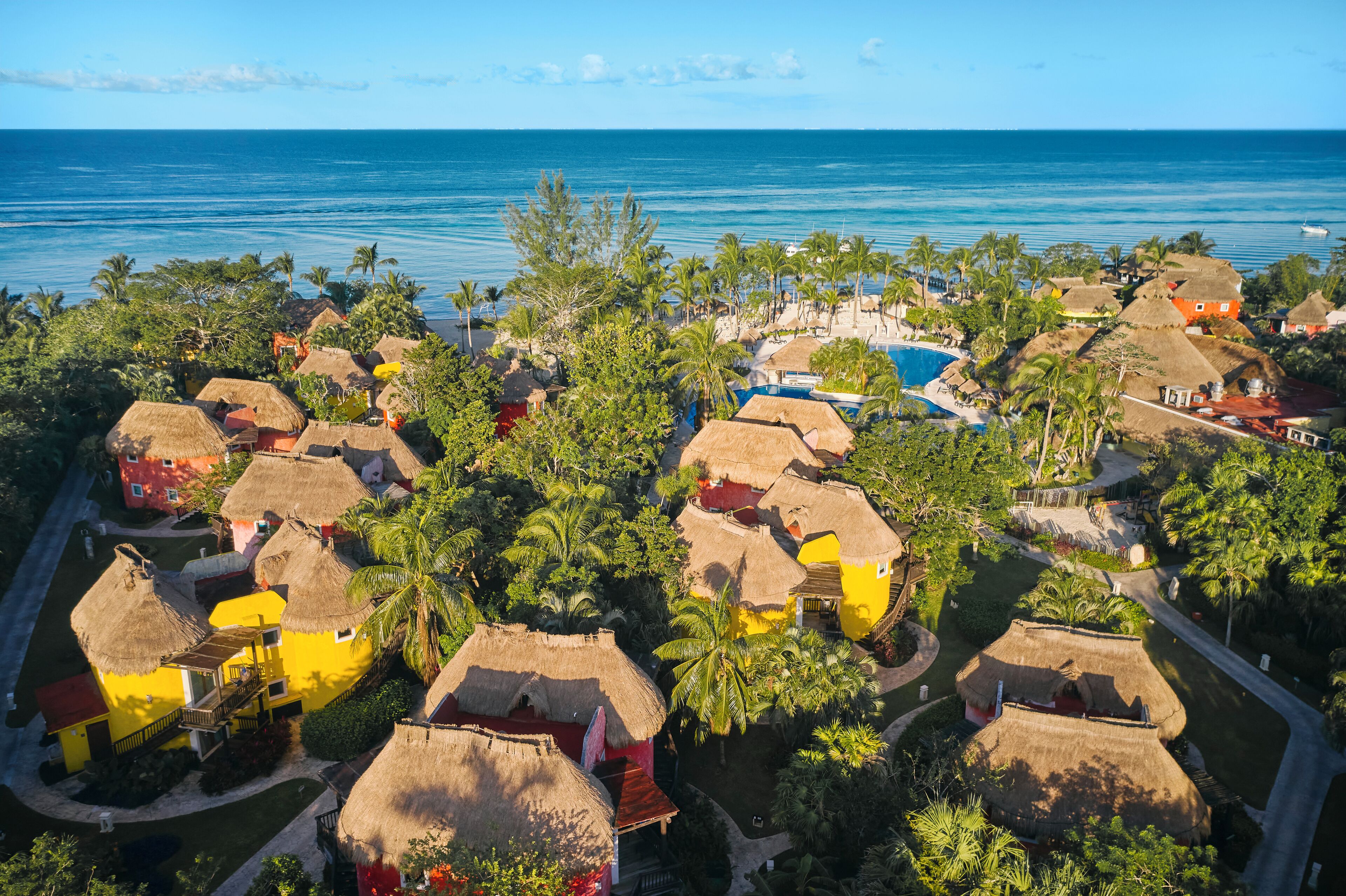 A resort with thatched-roof cottages, a swimming pool, and a view of the ocean.