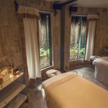 A spa room with two beds, a vanity, and a window with curtains.