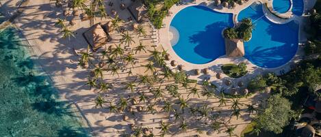An aerial view of a resort with a large pool, palm trees, and a beach area.