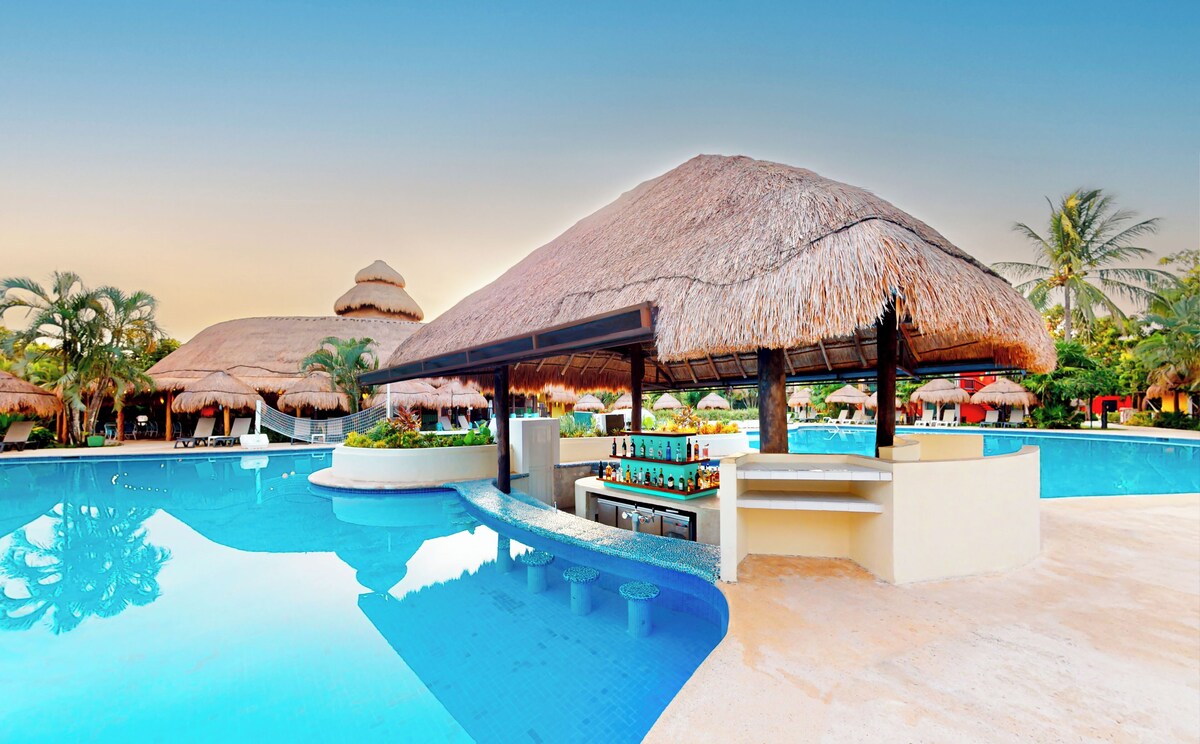 Relax by the pool surrounded by palm trees and thatched-roof structures.