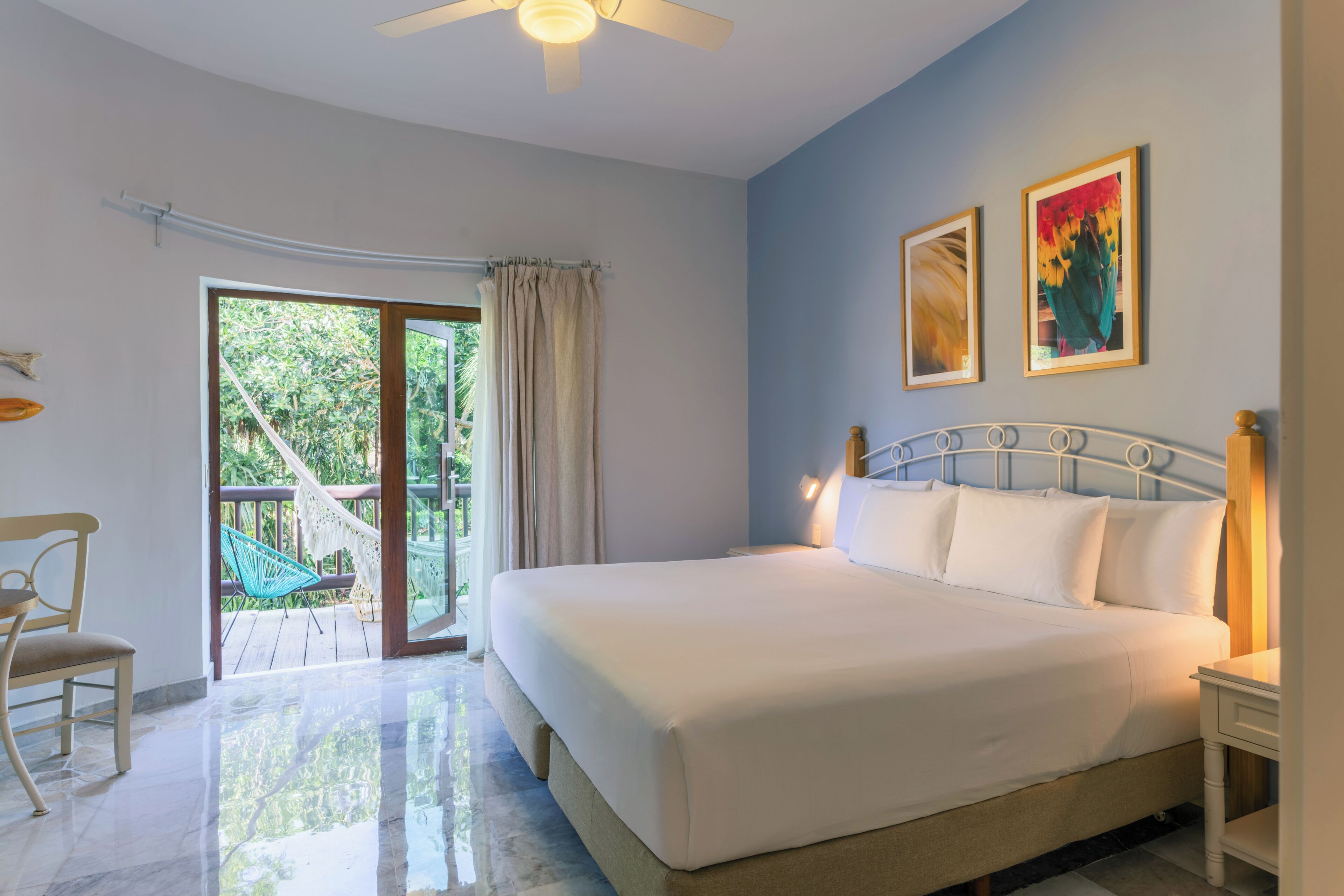 A bedroom with a bed, a chair, a ceiling fan, and a view of the outdoors.