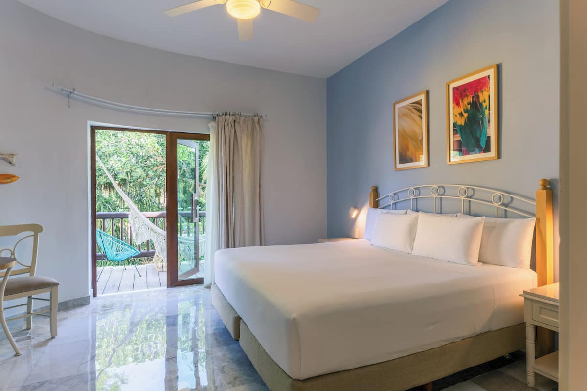 A bedroom with a bed, a chair, a ceiling fan, and a view of the outdoors.