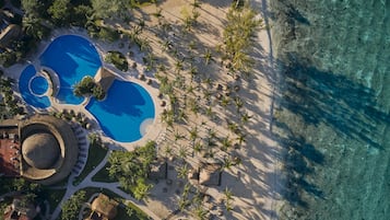 Vista aérea de un complejo turístico con una amplia piscina, palmeras y una zona de playa.