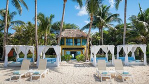 A beach resort with a thatched-roof building, white canopies, and lounge chairs with blue cushions. - Iberostar Waves Cozumel - All Inclusive (Cozumel)