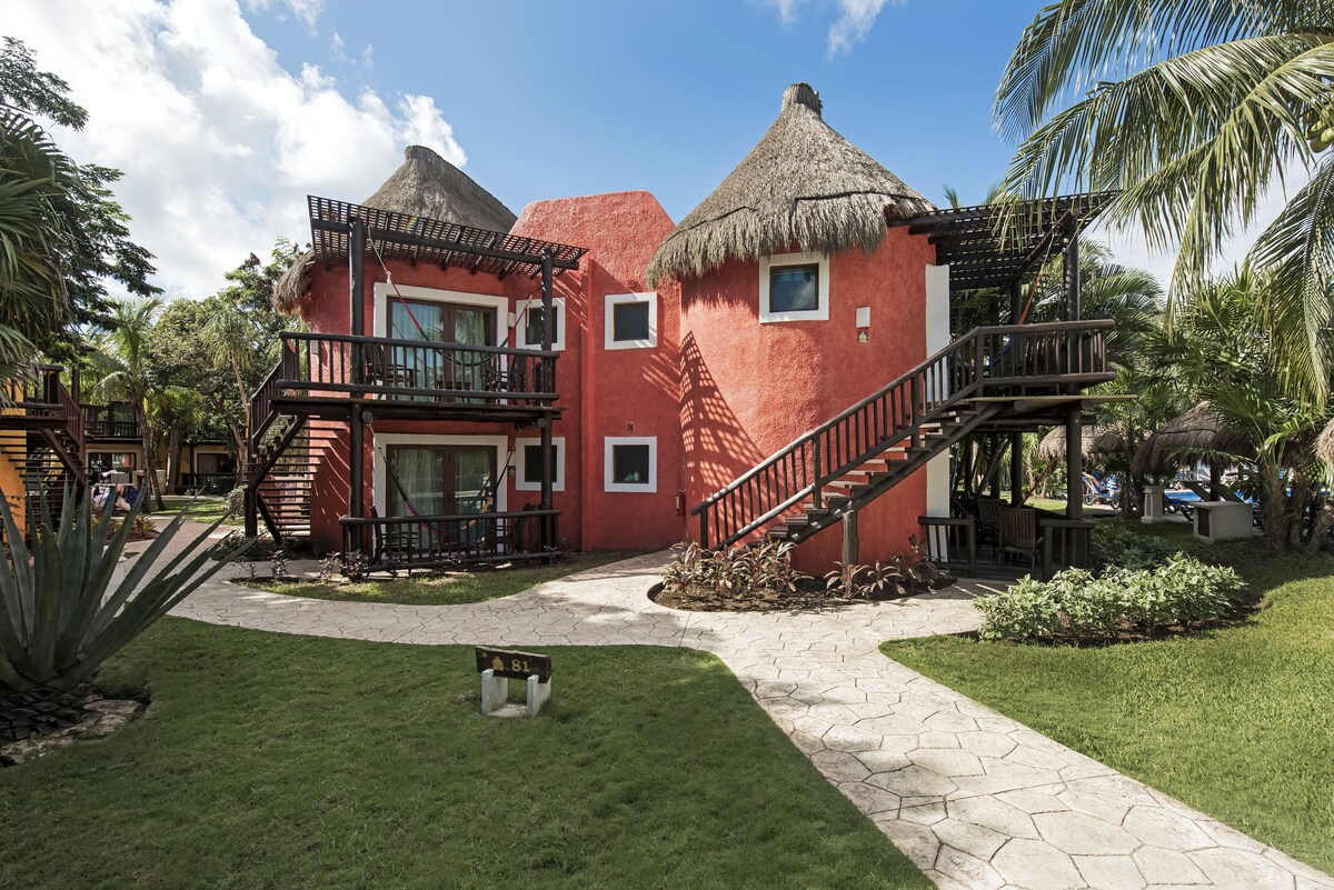 A rust colored villa is surrounded by lush green grass and palm trees.
