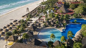Un resort con playa, piscina y construcciones de techo de paja.