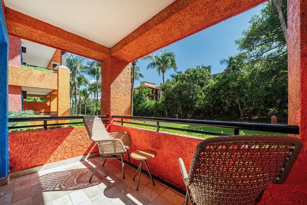 A balcony with wicker chairs, a small table, and a view of greenery and buildings.