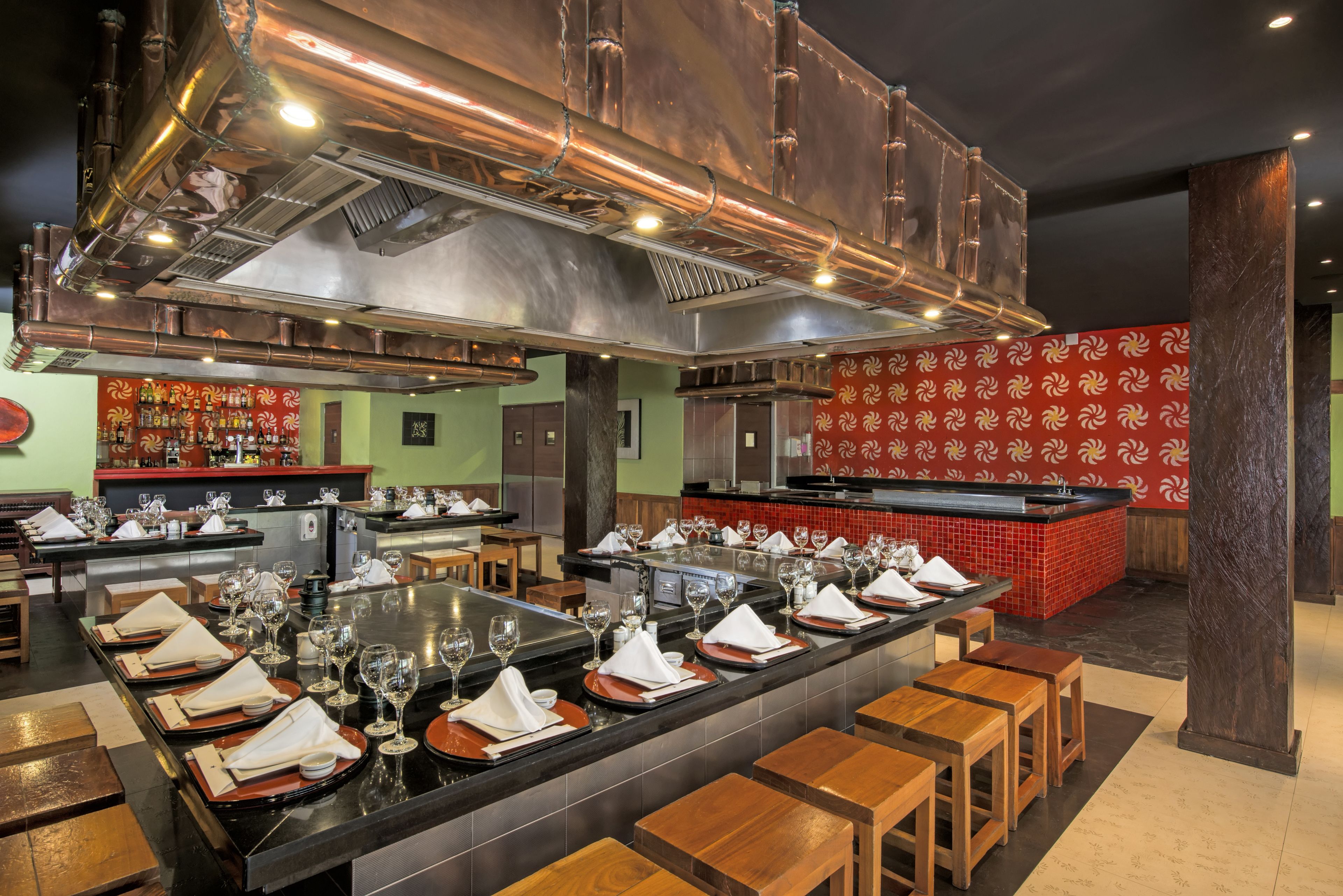 A restaurant with a central bar area, multiple seating options, and a distinctive red patterned wall.