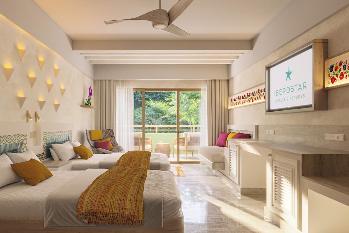 A hotel room with two beds, a ceiling fan, a TV, and a balcony with a view of greenery.