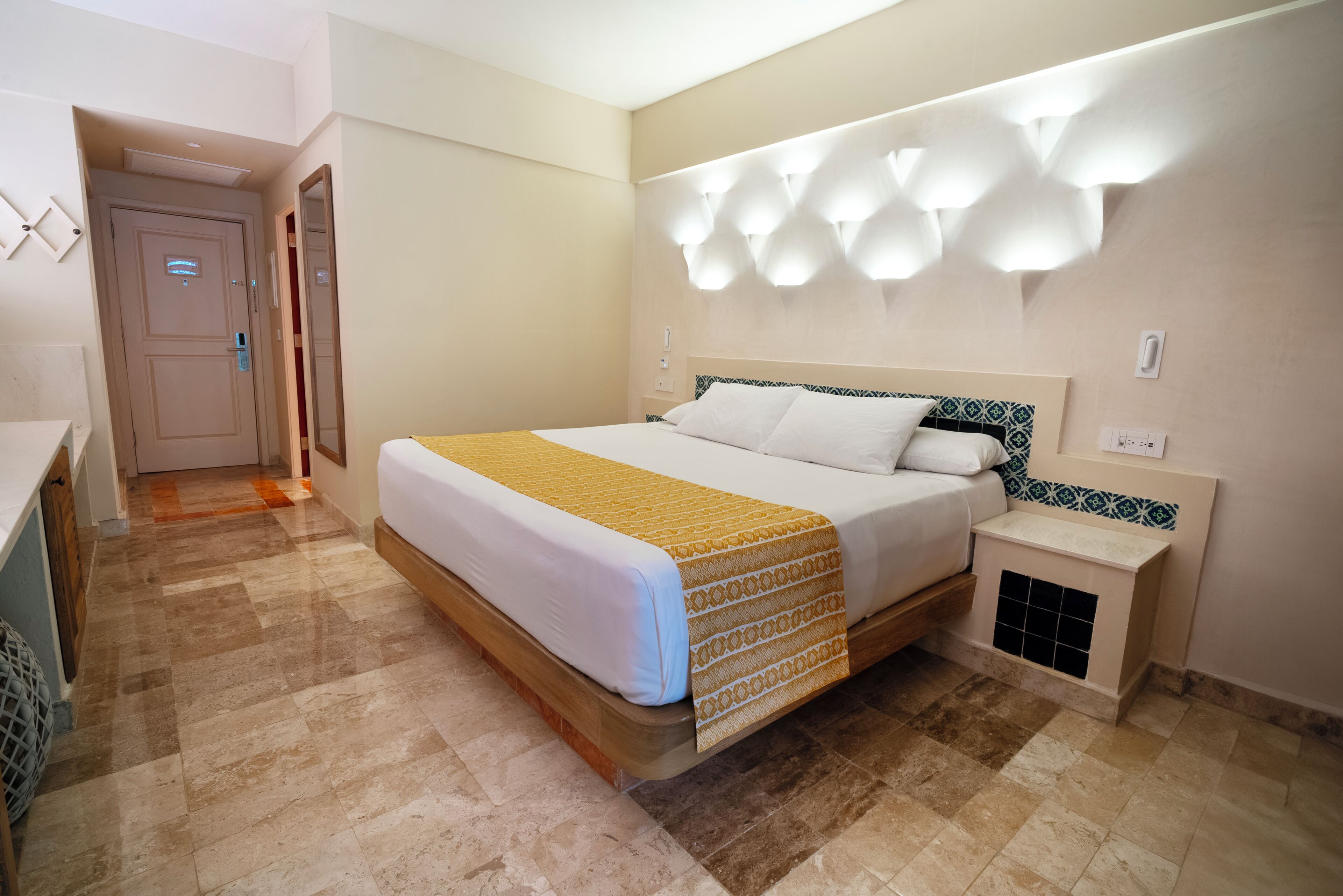 A hotel room with a bed, bedside table, and a wall-mounted light fixture.