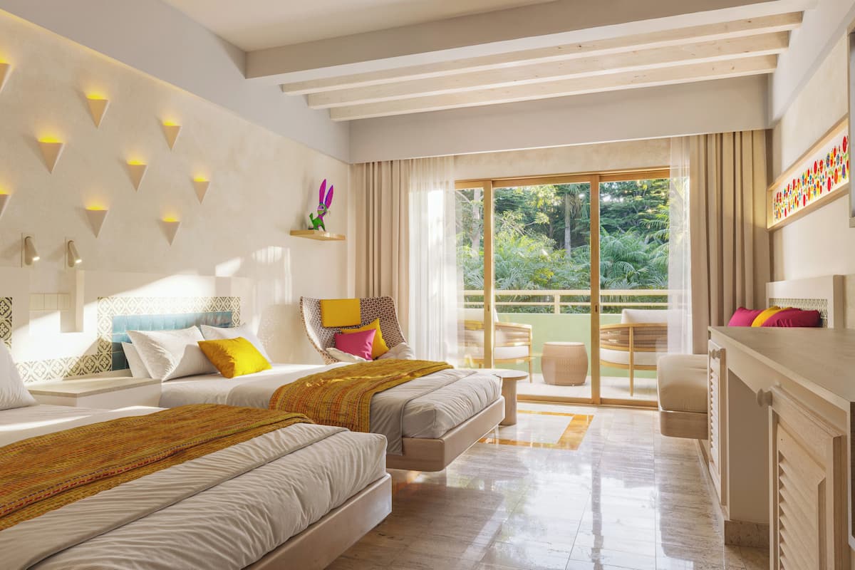 A modern hotel room with two beds, a balcony, and a view of greenery.