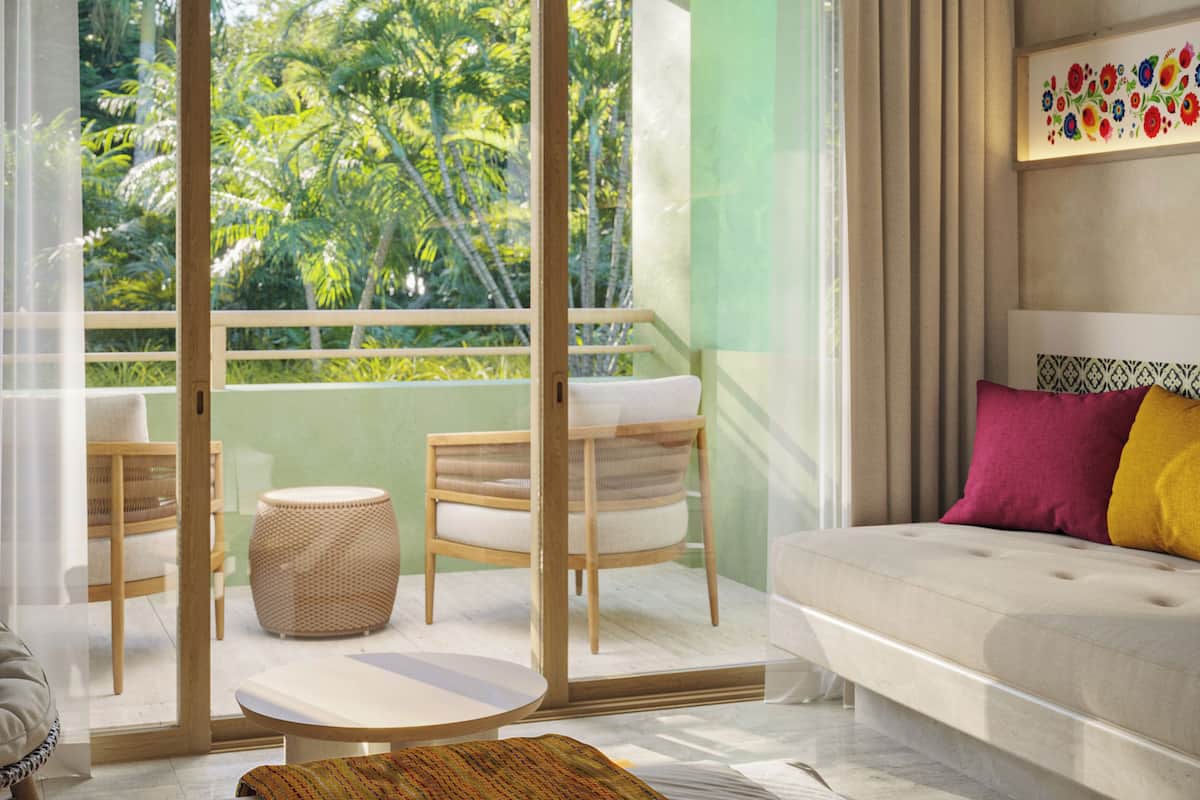 A room with a sofa, a chair, a small table, and a view of greenery through a glass door.