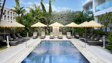 Relax by the pool surrounded by lush tropical plants and lounge chairs.