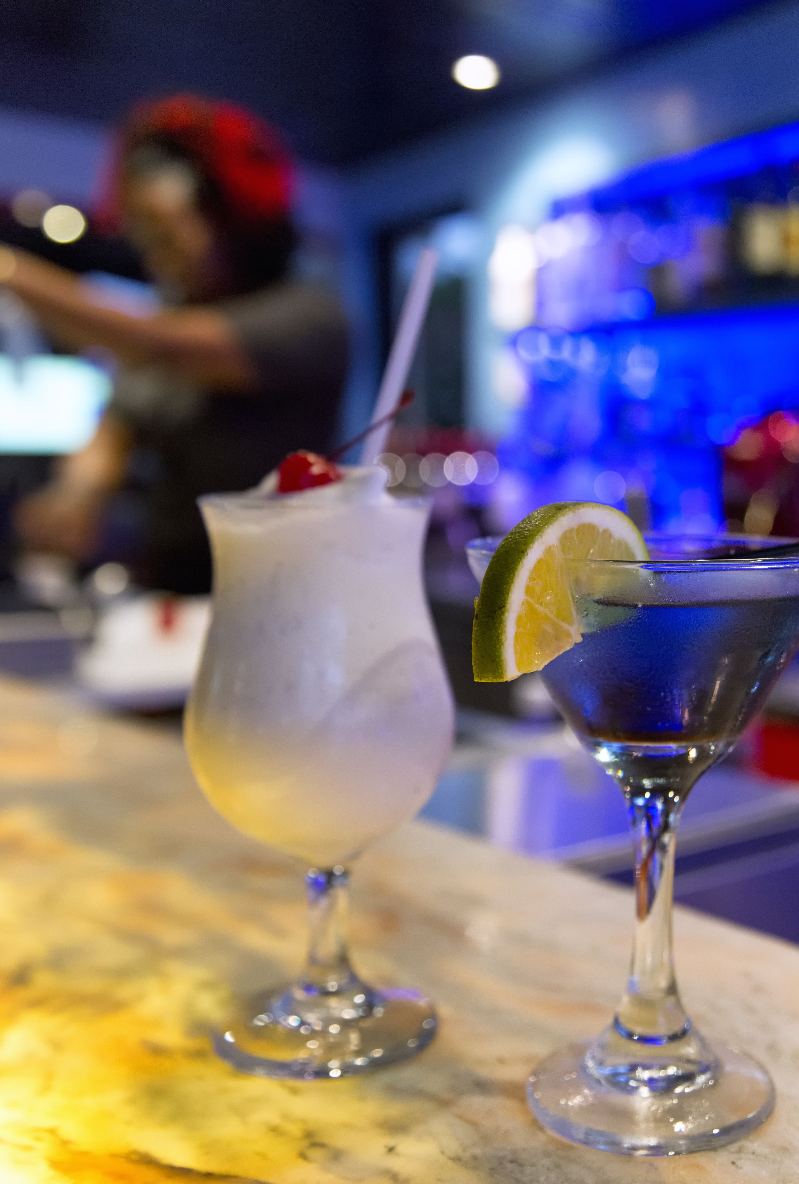 Two cocktails on a bar counter with a blurred background.