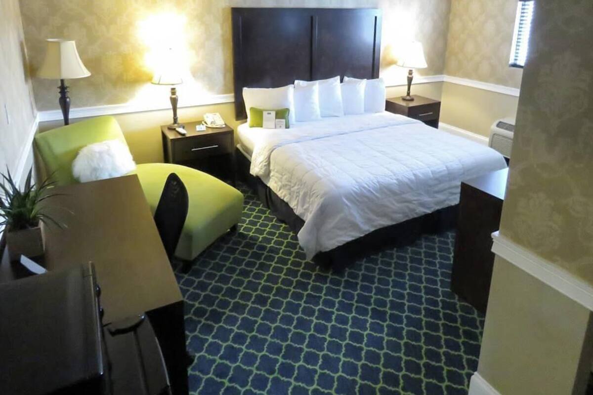 A hotel room with a bed, bedside tables, lamps, a chair, and a small table.