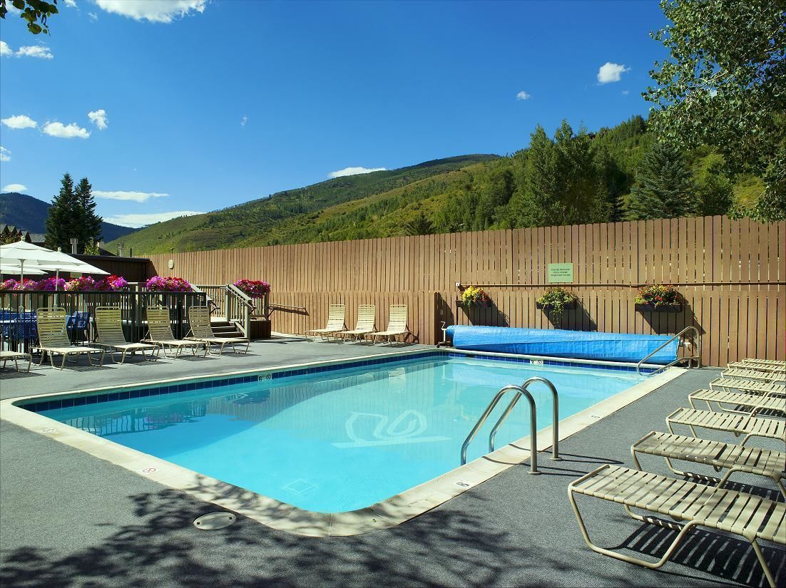A swimming pool with lounge chairs and umbrellas, surrounded by a wooden fence and trees.