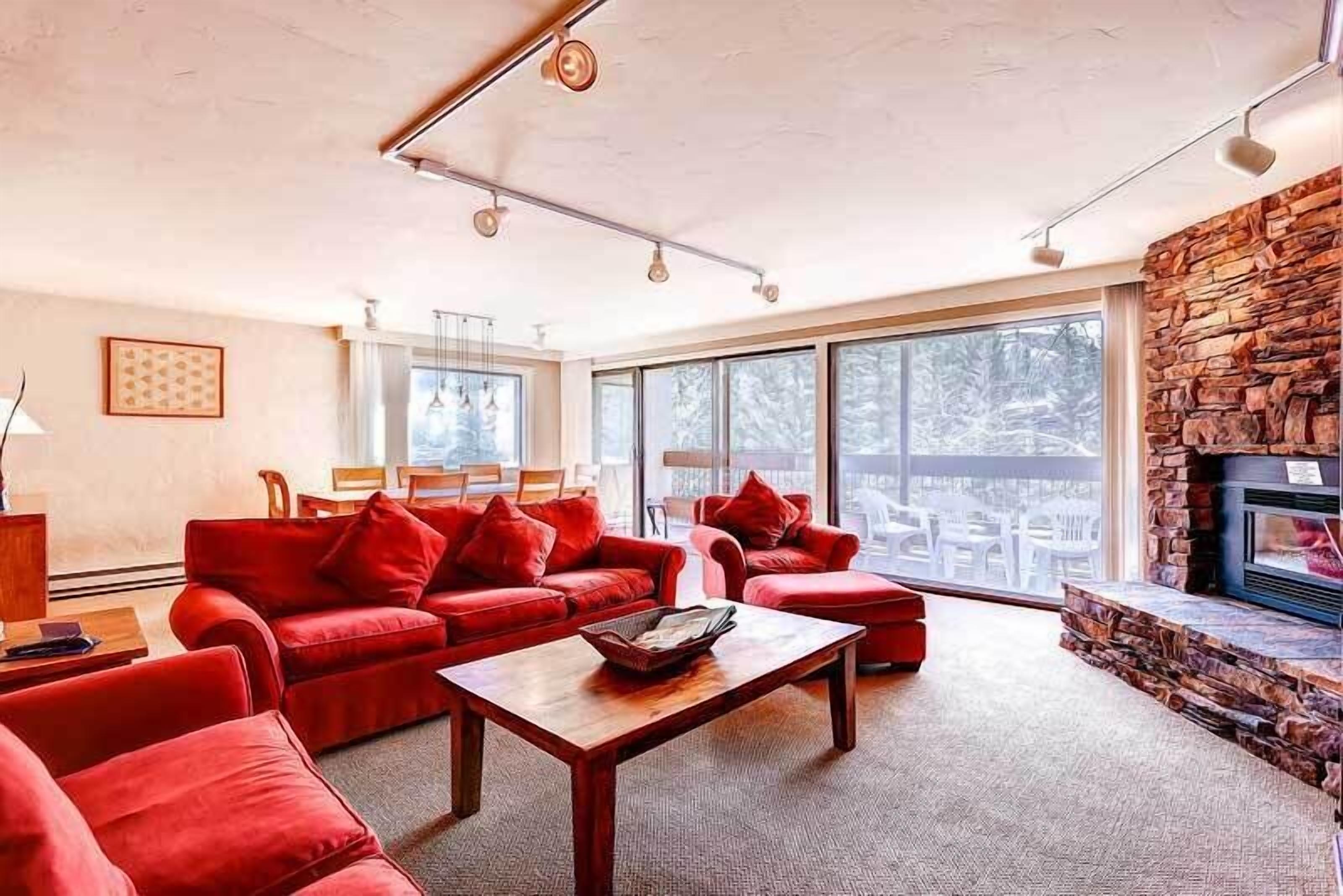 A spacious living room with red sofas, a wooden coffee table, and a stone fireplace.