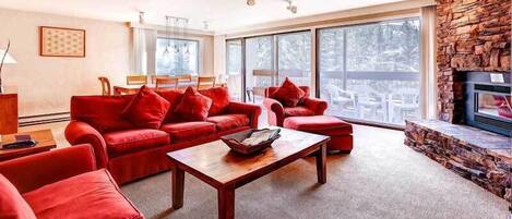 A spacious living room with red sofas, a wooden coffee table, and a stone fireplace.