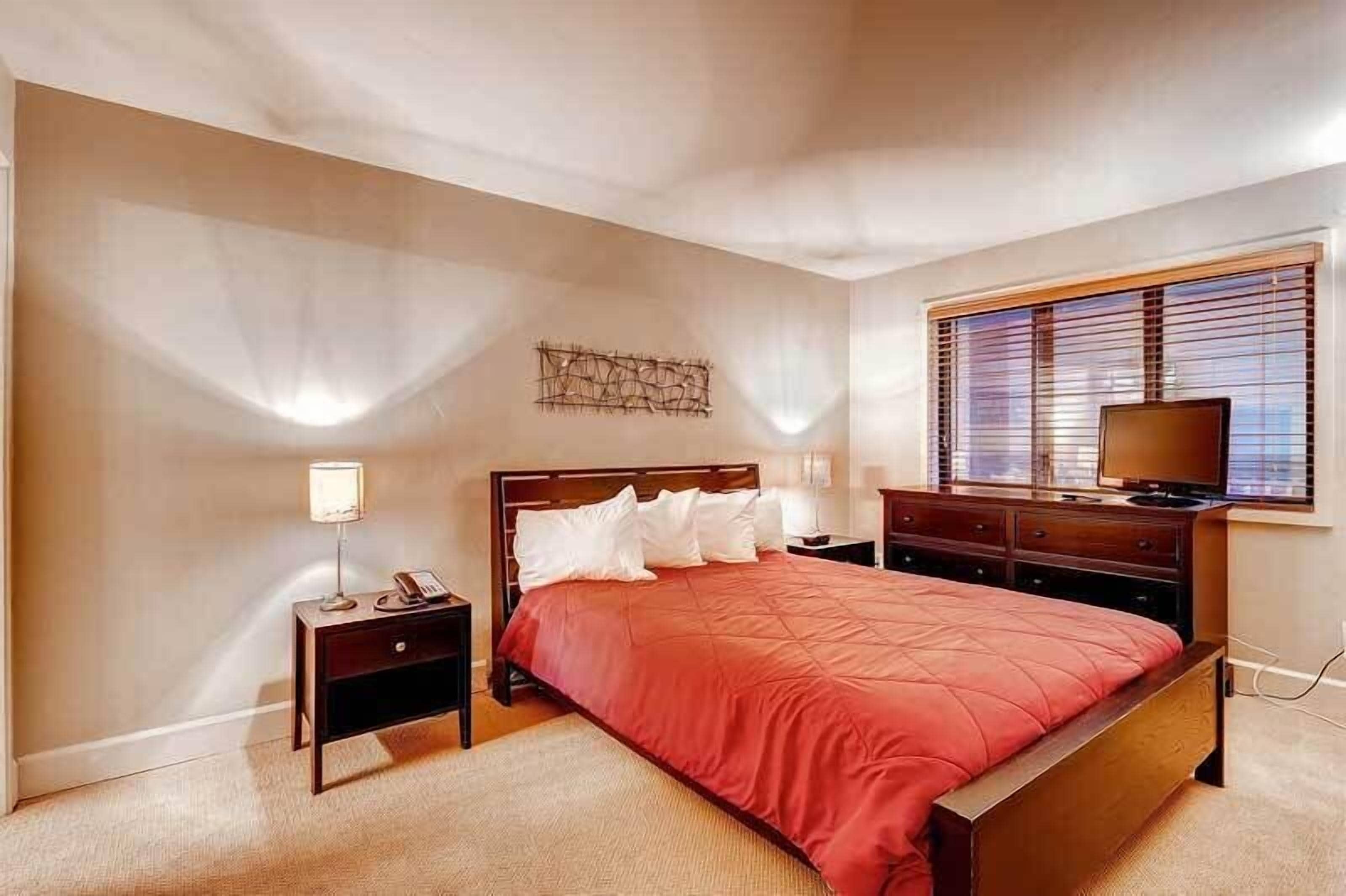 Une chambre à coucher avec un grand lit, une table de chevet, une commode et un téléviseur.