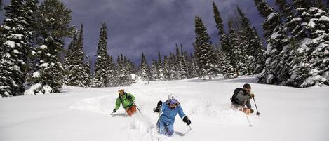 A snowy landscape with three skiers skiing down a slope.