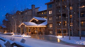 Un gran edificio de estilo lodge con varios pisos, una entrada cubierta de nieve y ventanas iluminadas.