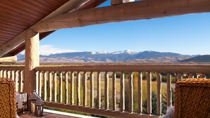 Una terraza de madera con sillas de mimbre y un farol, con vista a un paisaje montañoso.