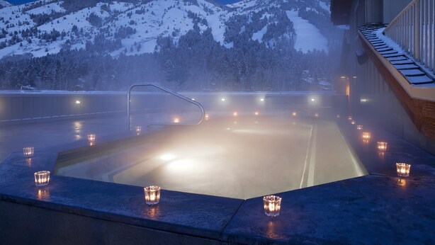 Un jacuzzi con velas, rodeado de montañas nevadas.