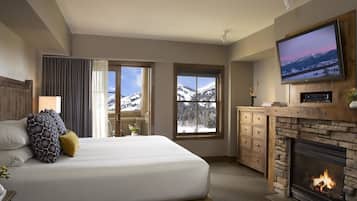 Una habitación de hotel con una cama grande, una chimenea, un televisor y vistas a montañas nevadas.